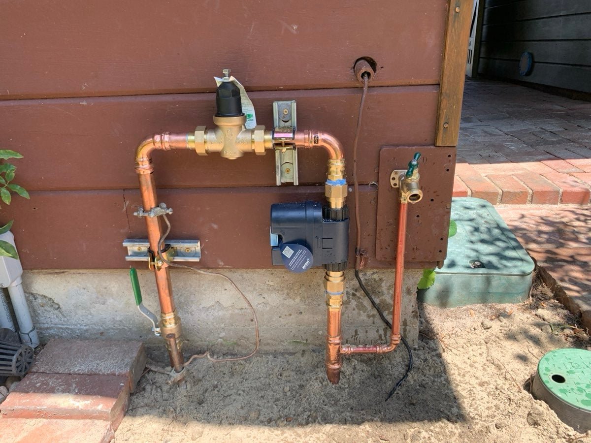 Copper main water line with pressure regulator on an exterior wall